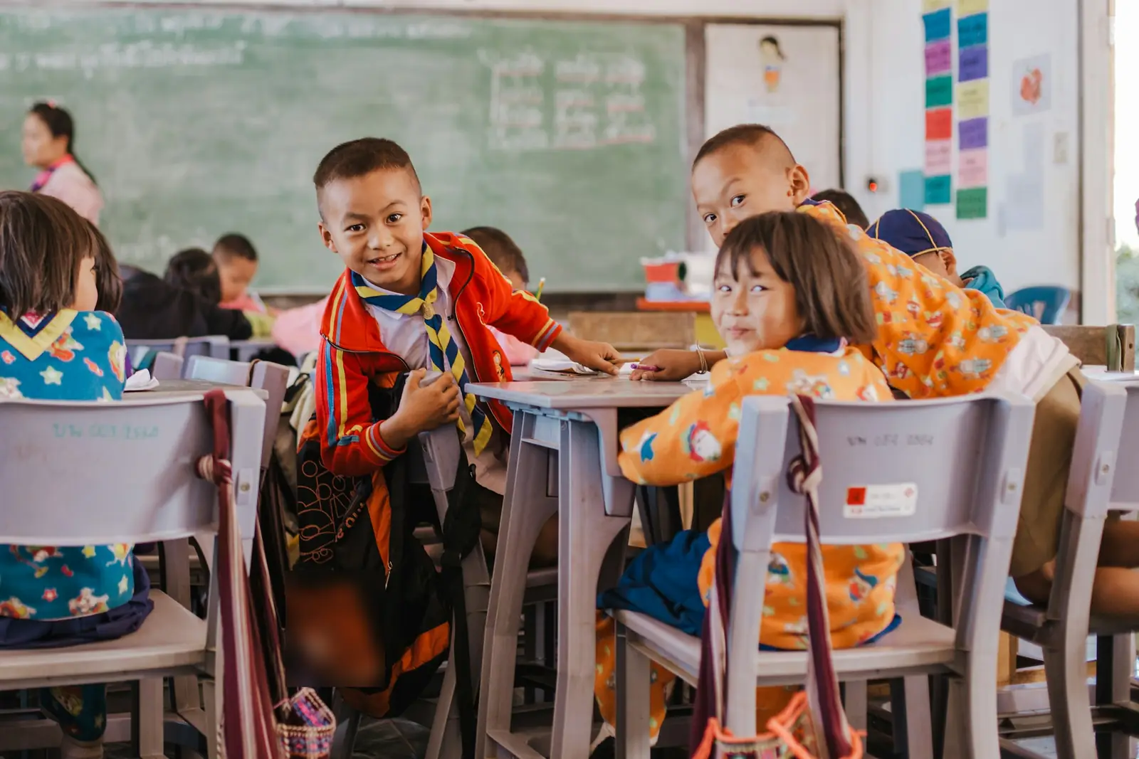 Smiling children at their desks with a teacher at the board